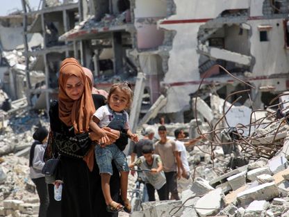 فلسطينية تحمل طفلها وسط ركام المباني التي دمرتها الضربات الإسرائيلية، خان يونس. 10 يوليو 2024 - Reuters