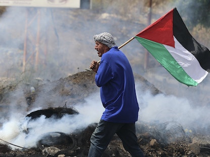 متظاهر يرفع علم فلسطين وسط مواجهات مع قوات الأمن الإسرائيلية على حاجز حوارة، جنوب مدينة نابلس بالضفة الغربية، 21 مايو 2021 - AFP