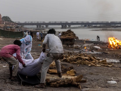 أشخاص يضعون جثة متوفي بسبب فيروس كورونا، في محرقة على ضفاف نهر الغانج بولاية أوتار براديش الشمالية - الهند - 6 مايو 2021 - REUTERS