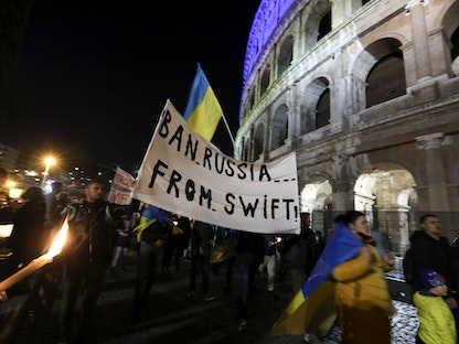لافتة تطالب بمنع روسيا من استخدام نظام "سويفت" خلال تظاهرة مؤيّدة لأوكرانيا أمام الكولوسيوم في روما - 25 فبراير 2022 - Bloomberg
