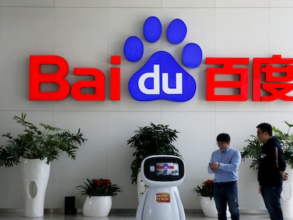 رجال يتفاعلون مع "روبوت" Baidu AI بالقرب من شعار الشركة في مقرها الرئيسي في العاصمة الصينية بكين. 23 أبريل 2021 - REUTERS