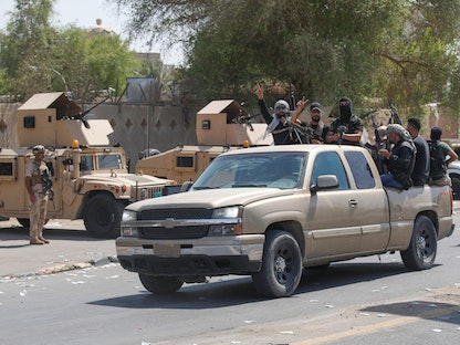 مسلحون من "سرايا السلام" التابعة للتيار الصدري خلال انسحابهم من المنطقة الخضراء في وسط بغداد يمرون أمام مجموعة من عناصر الجيش العراقي. 30 أغسطس 2022 - AFP