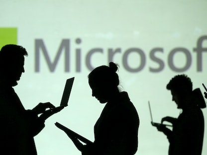 صورة توضيحية لأشخاص يحملون حواسيب أمام شعار "مايكروسوفت" - REUTERS