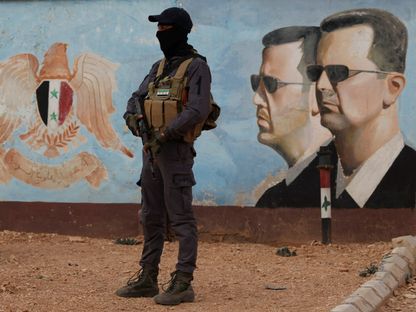 مسلح تابع للإدارة السورية الجديدة يقف في نوبة حراسة بالقرب من صورة للرئيس السابق بشار الأسد في مقر الفرقة الرابعة بدمشق. 23 يناير 2025 - رويترز