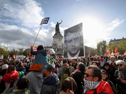 متظاهر يحمل لافتة عليها صورة الرئيس الفرنسي إيمانويل ماكرون ومكتوب عليها كلمة - AFP