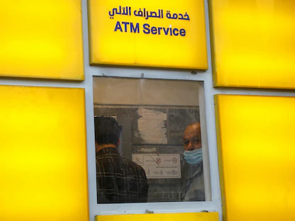 موظف حكومي في السلطة الفلسطينية ينظر عبر نافذة بينما ينتظر تسلم راتبه عن طريق ماكينة صراف آلي خارج أحد البنوك في الضفة الغربية المحتلة، 3 ديسمبر 2020 - REUTERS