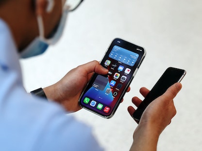 مستخدم يحمل هاتف "آيفون 12" في أحد متاجر "أبل" في أستراليا - Bloomberg