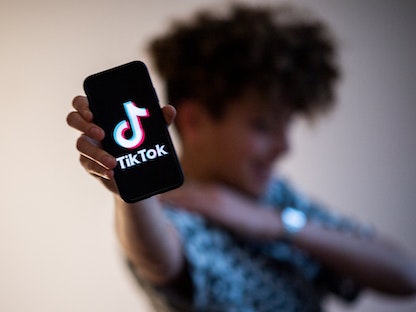 مراهق يحمل هاتفاً ذكياً عليه شعار تطبيق "تيك توك" - AFP