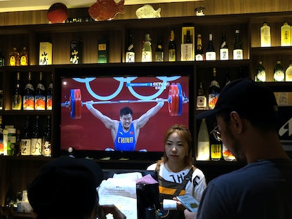 الرياضي الصيني ليو شياو جون يظهر على شاشة تلفزيون خلال مشاركته في مسابقة رفع الأثقال للرجال خلال أولمبياد طوكيو في مطعم بالعاصمة اليابانية بكين - X06979