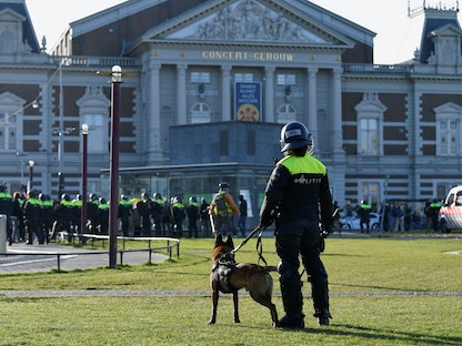 ضابط شرطة بصحبة كلب بوليسي بالقرب من مظاهرة احتجاجاً على قيود مرض كورونا في أمستردام، هولندا. 21 فبراير 2021. - REUTERS