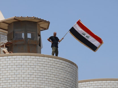 أحد المتظاهرين من أنصار "التيار الصدري" يلوح بعلم العراق، بينما يقف على برج مراقبة بمبنى البرلمان في بغداد- 30 يوليو 2022 - AFP