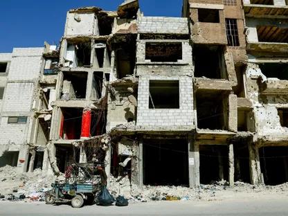 مركبة بثلاث عجلات محملة بالقمامة والأمتعة أمام مبنى متضرر في مخيم اليرموك للاجئين في دمشق- 22 سبتمبر 2025 - Reuters