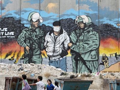 أطفال فلسطينيون يسيرون بجانب الجدار العازل المثير للجدل الذي يفصل المناطق الإسرائيلية عن الضفة الغربية- 14 مايو 2012 - REUTERS