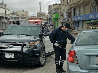 رجل أمني أردني يتحدث إلى سائق سيارة في العاصمة عمان خلال الحظر المفروض لاحتواء انتشار فيروس كورونا 21 مارس 2020 - AFP