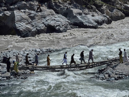 عدد من الأشخاص يعبرون جسراً مؤقتاً للمشاة وسط فيضانات تسببت فيها سيول عارمة ضربت باكستان. 31 أغسطس 2022 - AFP