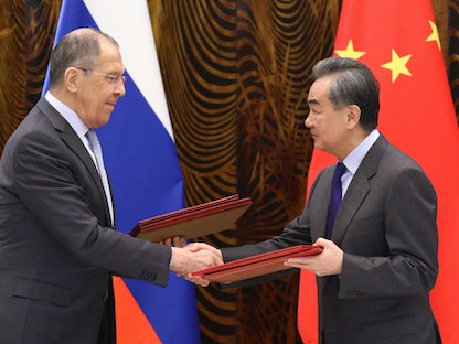وزير الخارجية الصيني، وانغ يي (يمين) ونظيره الروسي سيرغي لافروف، يتبادلان الوثائق خلال حفل توقيع عقب محادثاتهما في قويلين - 23 مارس 2021 - AFP
