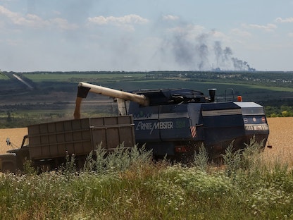 مزارعون يحصدون القمح في الوقت الذي تحترق فيه محطة فولهيرسك لتوليد الطاقة الحرارية بمنطقة دونباس بأوكرانيا - 18 يوليو 2022 - REUTERS