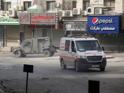 سيارة إسعاف فلسطينية وآلية عسكرية إسرائيلية خلال مواجهات في جنين بالضفة الغربية المحتلة. 22 مايو 2024 - Reuters