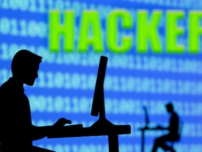 كلمة Hacker - تعني مخترقاً - في خلفية شخص يظهر جالساً على جهاز كمبيوتر - REUTERS