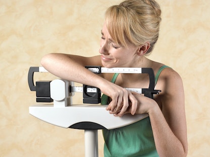 امرأة متكئة على ميزان وتبدو غير راضية عن وزنها. - Getty Images