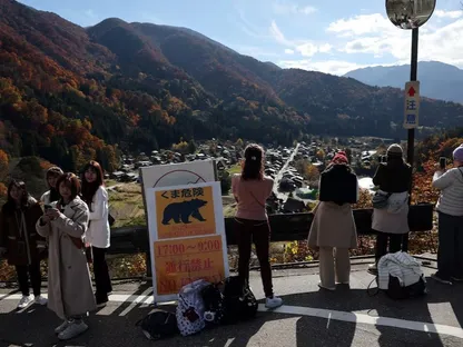 أشخاص يلتقطون صوراً تذكارية بجوار لافتة تحذر من هجمات الدببة، في أحد مواقع التراث العالمي، قرية شيراكاوا، جيفو، اليابان. 15 نوفمبر 2025 - Reuters
