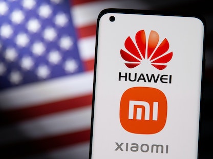 رسم توضيحي يُظهر هاتفاً ذكياً بشعارات Huawei و Xiaomi أمام علم الولايات المتحدة - REUTERS