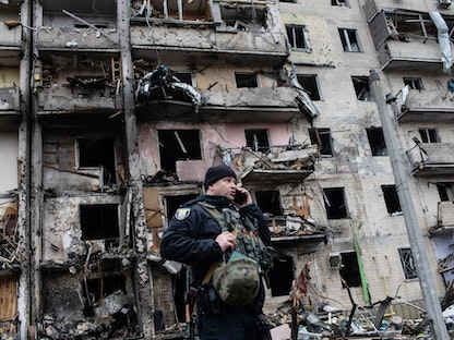 شرطي أوكراني أمام مبنى استهدفه قصف مدفعي روسي في كييف - 25 فبراير 2022 - Bloomberg