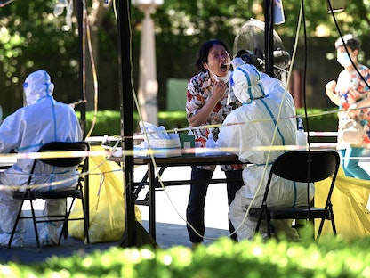 عامل صحي (يمين) يأخذ عينة من امرأة لفحصها للكشف عن فيروس كورونا Covid-19 في بكين- 5 يونيو 2022  - AFP