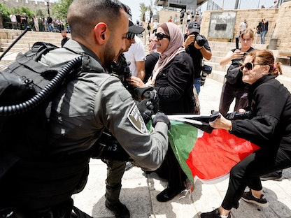 جندي إسرائيلي يحاول نزع علم فلسطين من سيدة فلسطينية خلال احتجاجات في القدس المحتلة - 29 مايو 2022  - REUTERS