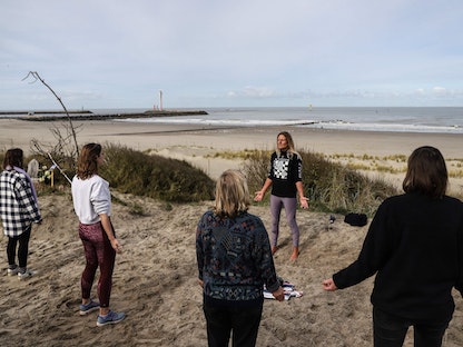 مجموعة من السيدات يمارسن رياضة التأمل قبل جلسة ركوب الأمواج في بلجيكا. 11 مارس 2023 - AFP