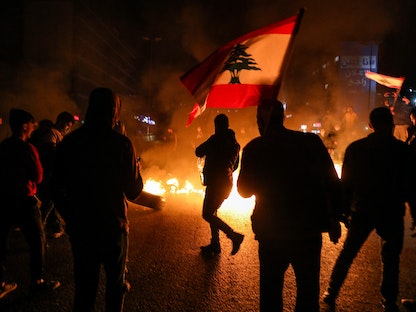 متظاهر يلوّح بالعلم اللبناني قرب إطارات مشتعلة تقطع طريقاً رئيسياً في العاصمة اللبنانية بيروت، 2 مارس - AFP
