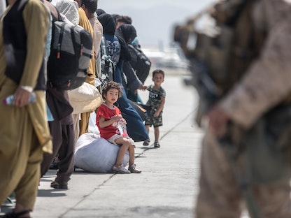طفلان ينتظران مع عائلتهما ركوب طائرة تابعة لسلاح الجو الأميركي أثناء عملية إجلاء في مطار كابول - 22 أغسطس 2021 - Samuel Ruiz via REUTERS