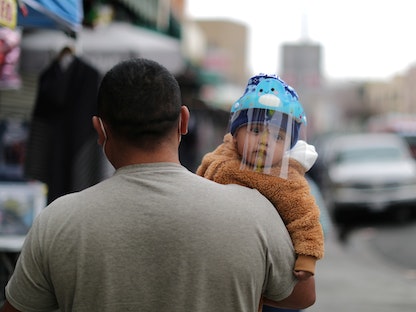 رجل يحمل طفلاً يرتدي قناعاً للوقاية من فيروس كورونا في لوس أنجلوس - REUTERS