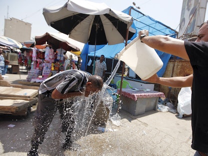 رجل في العاصمة العراقية بغداد يصب دلواً من الماء على رأس آخر خلال يوم صيفي حار. 30 يوليو 2015  - REUTERS