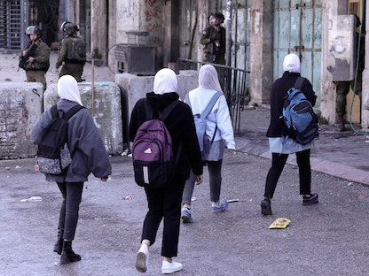 طلاب يسيرون وسط اشتباكات بين المتظاهرين الفلسطينيين وقوات الأمن الإسرائيلية في بلدة الخليل بالضفة الغربية - 1 مارس 2022 - AFP
