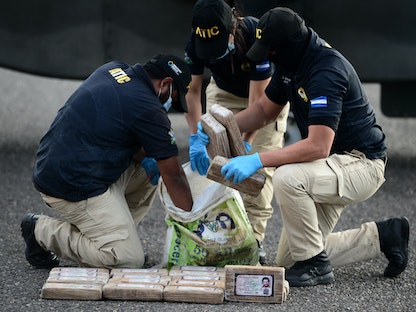 أعضاء وكالة التحقيقات الجنائية الهندوراسية يزيلون عبوات الكوكايين من كيس عليه بطاقة هوية لتاجر المخدرات الكولومبي التاريخي بابلو إسكوبار. - AFP