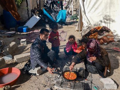 أسرة فلسطينية تحاول طهو الطعام أمام منزلهم الذي دمرته غارة إسرائيلية على رفح في جنوب قطاع غزة. 11 ديسمبر 2023 - AFP