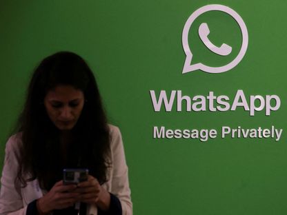 سيدة تستخدم هاتفها بجوار شعار تطبيق واتساب خلال فعالية تقنية في الهند. 20 سبتمبر 2022 - REUTERS