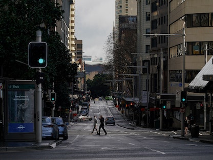 مشاة يعبرون شارعاً هادئاً بشكل غير معتاد أثناء الإغلاق للحد من انتشار فيروس كورونا في سيدني. أستراليا - 29 يونيو 2021 - REUTERS