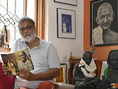 توشار غاندي نجل حفيد المهاتما غاندي يحمل كتاباً خلال مقابلة مع "فرانس برس" في منزله بمدينة مومباي. 25 يناير 2023 - AFP