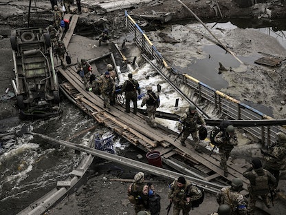 عناصر من الجيش الأوكراني تعبر جسراً حطمه القصف الروسي في مدينة إربين بالقرب من العاصمة كييف - 13 مارس 2022 - AFP
