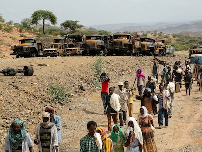 سكان من إقليم تيجراي يمشون أمام عشرات المركبات المحترقة، تيجراي، إثيوبيا، 10 يوليو 2021 - REUTERS