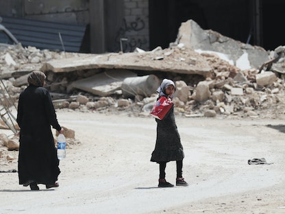 امرأة وفتاة تمران قرب أنقاض مبانٍ مدمرة في بلدة النيرب بمحافظة إدلب، 17 أبريل 2020 - REUTERS