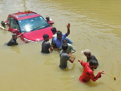 أشخاص يسحبون سيارة عبر طريق مليء بالمياه بعد هطول أمطار غزيرة في بنجالورو - REUTERS