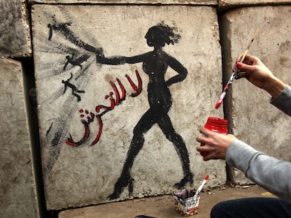 ناشط حقوقي مصري يرسم امرأة وإلى جانبها عبارة "لا للتحرش الجنسي" على جدار خارج القصر الرئاسي في القاهرة، 14 ديسمبر 2012 - AFP