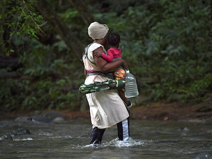 مهاجرة من هايتي تحمل طفلاً أثناء عبورها غابة دارين بالقرب من أكاندي في مقاطعة تشوكو بكولومبيا في طريقها إلى بنما - 26 سبتمبر 2021. - AFP