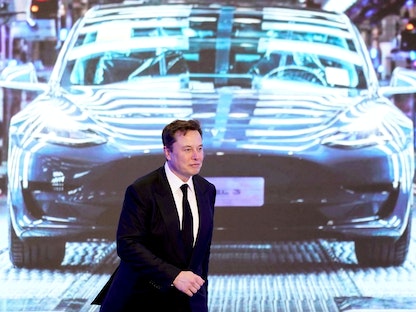 الرئيس التنفيذي لشركة تسلا، إيلون ماسك، يسير بجوار شاشة تعرض صورة لسيارة "Tesla Model 3" في شنغهاي بالصين، 7 يناير 2020 - REUTERS