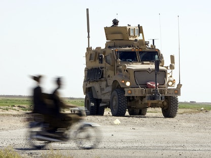 رجال أفغان يركبون دراجة نارية بجوار مدرعة تابعة للجيش الأميركي عند نقطة تفتيش للشرطة الأفغانية خارج قندهار جنوب أفغانستان، 25 مارس 2010 - REUTERS