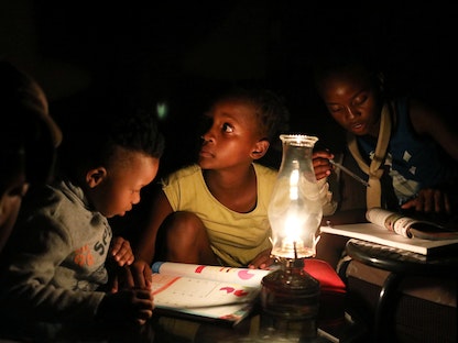 أطفال يرجعون دروسهم على ضوء مصباح "البارافين" أثناء انقطاع التيار الكهربائي في سويتو بجنوب إفريقيا. 18 مارس 2021 - REUTERS