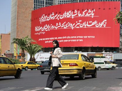 سيدة إيرانية في أحد شوارع طهران أمام لوحة تحمل رسائل معادية لإسرائيل. 15 يونيو 2025 - Reuters